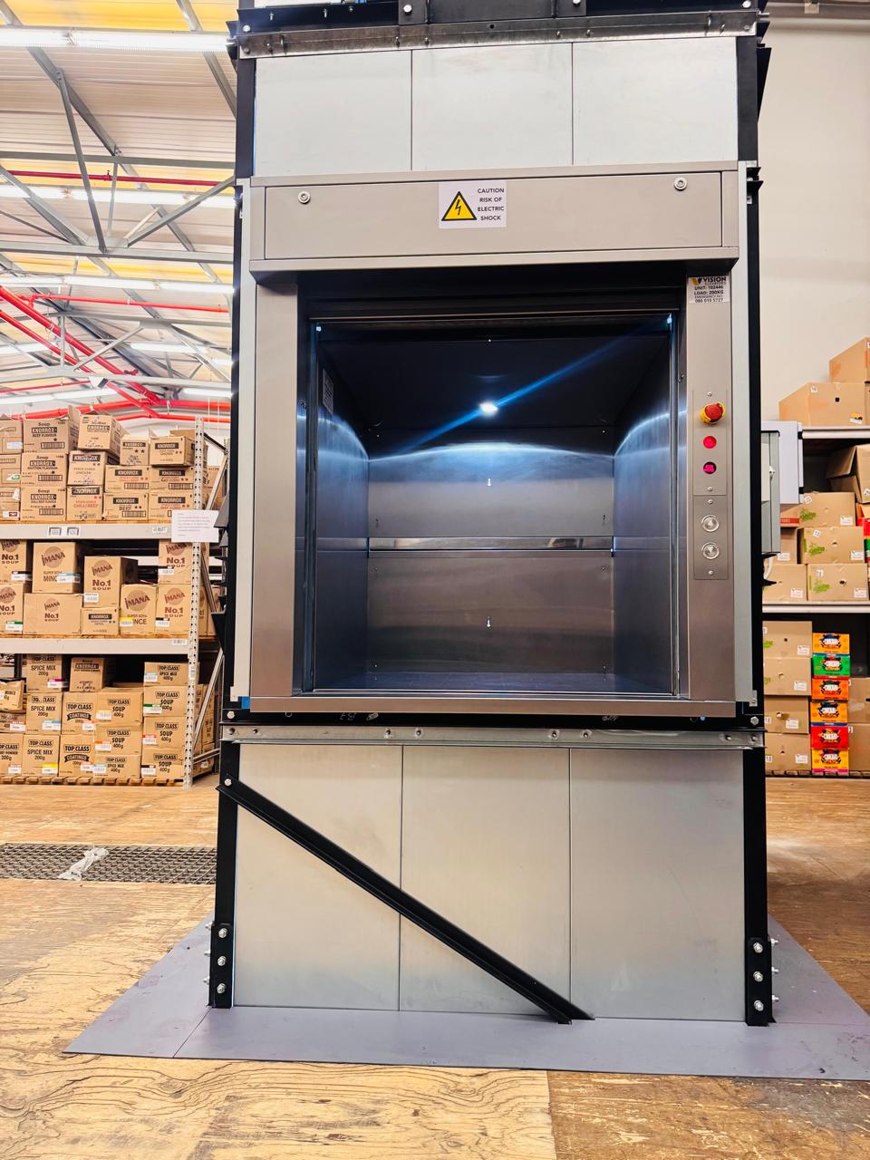 Dumbwaiter with an open loading compartment beside stocked storage shelves.