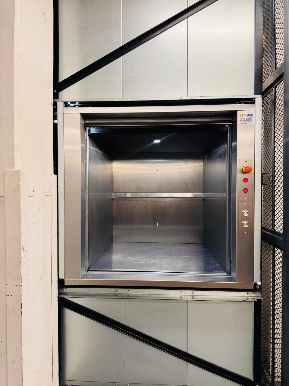 Open dumbwaiter loading compartment with side controls and an emergency-stop button.