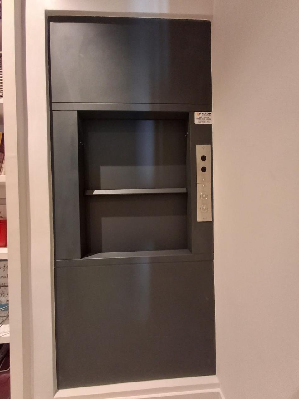 Recessed dumbwaiter entrance with a dark surround and side-mounted controls.
