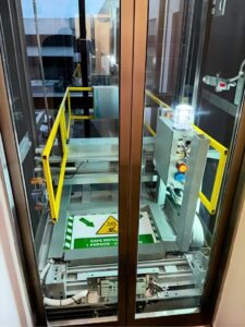 Lift controller and safety-gate detail beside the glass passenger-elevator shaft.