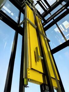 Yellow guide-rail assembly inside the glazed passenger-elevator shaft.
